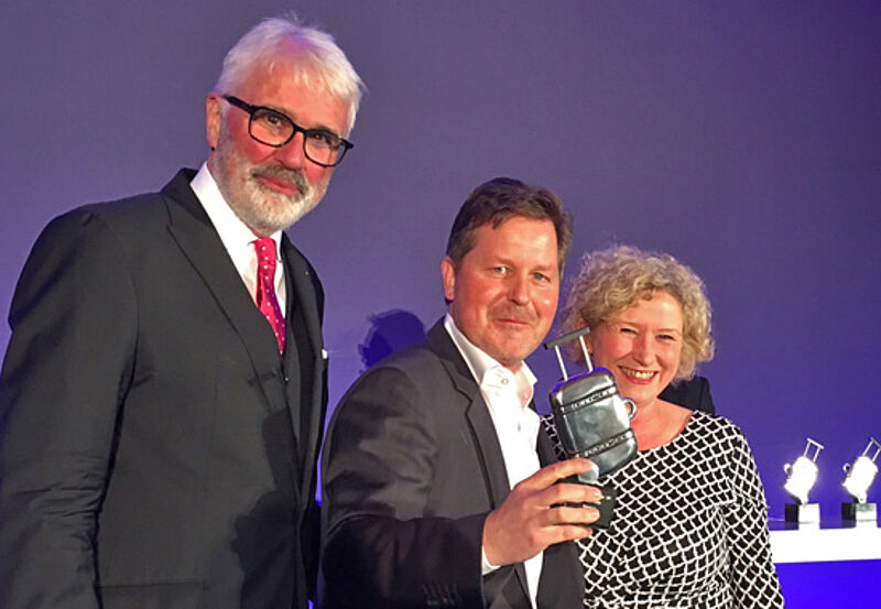 Preisträger Thorsten Lehmann (Mitte) mit TVG-Chefin Birgit Aust und Jury-Chef Peter Agel auf der TIC-Bühne in Köln