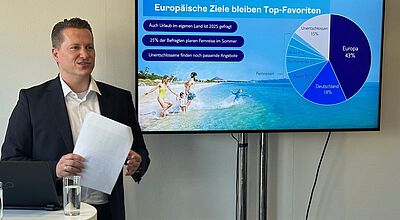Mann steht an Stehtisch, daneben ein Bildschirm auf die Ergebnisse einer Umfrage zu europäischen Reisezielen gezeigt werden