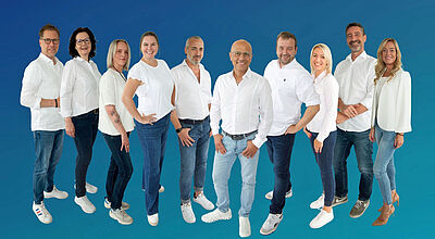 Die neuen Außendienst-Mitarbeiter mit Ender Karadag, Vertriebsleiter Coral Travel/Ferien Touristik, und Stefan Heimerl, Senior Manager Sales and Distribution Gruppe von Menschen vor einem blauen Hintergrund