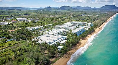 Ein großes weißgetünchten Hotelgebäude liegt einsam an einem langen Sandstrand