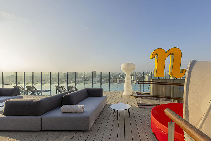 Blick über eine Dachterrasse mit Lounge-Möbeln, ein großes N zeigt die Marke Nhow an. Im Hintergrund kann man Lima erahnen.