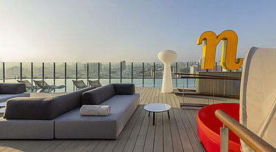 Blick über eine Dachterrasse mit Lounge-Möbeln, ein großes N zeigt die Marke Nhow an. Im Hintergrund kann man Lima erahnen.