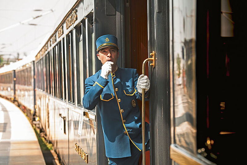 Zugbegleiter in eleganter Uniform signalisiert mit Trillerpfeife die Abfahrt eines historischen Luxuszuges