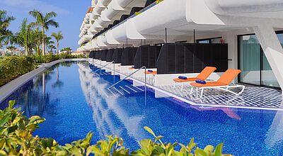 Ein modernes weißes Resort, im Erdgeschoss Zimmer mit Terrassen, vor denen sich ein schmaler Pool langzieht