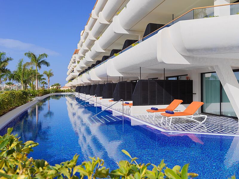 Ein modernes weißes Resort, im Erdgeschoss Zimmer mit Terrassen, vor denen sich ein schmaler Pool langzieht