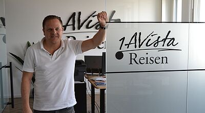 Ein Mann mittleren Alters in weißem Poloshirt posiert vor seinem modernen Büro und hat den Arm lässig an eine Glastür gelehnt.