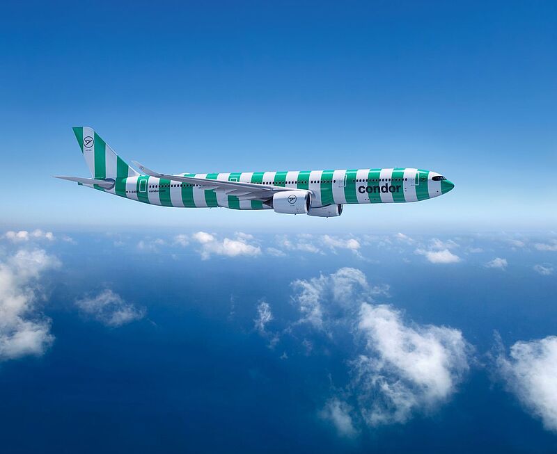   Ein Airbus A330-900neo der Fluggesellschaft Condor in grüner und weißer Streifenlackierung („Island“-Design) fliegt über den Wolken bei blauem Himmel.