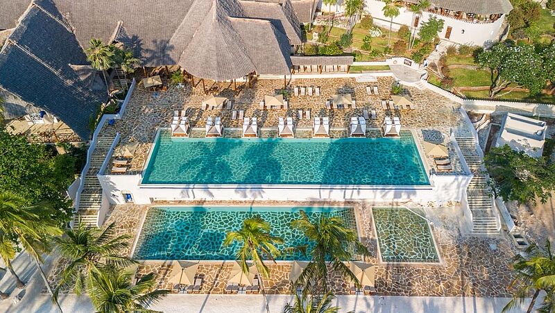 Luxuriöse Hotelanlage mit großen Pools, Sonnenliegen und Palmen im tropischen Urlaubsziel Sansibar – ein guter Ort zum Entspannen mit Blick auf den Indischen Ozean.