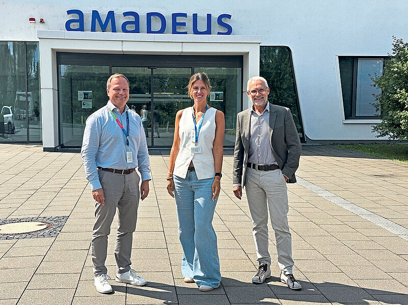 Standen touristik aktuell Rede und Antwort (von links): Amadeus-Manager Oliver Rengelshausen, Ljiljana Budalic und Klaus Ennen. Foto: mg Drei Personen stehen lächelnd vor dem Eingang eines Gebäudes mit dem Schriftzug ‚Amadeus‘. Es ist ein sonniger Tag, die Personen tragen Bürokleidung mit sichtbaren Namensschildern.
