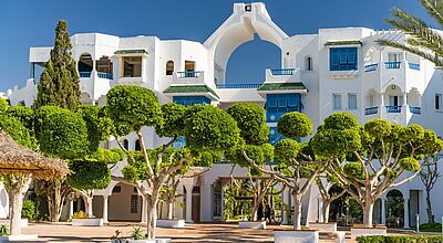 Hinter grünen Bäumen steht ein weißes Hotelgebäude