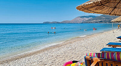 Ein Strand mit Sonnenschirmen und Liegestühlen mit Blick auf das Meer mit Badegästen