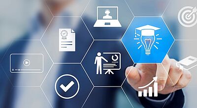 Um dem Fachkräftemangel entgegenzuwirken, hat die Reisebüro-Kooperation RTK eine Kooperation mit der IU Hochschule gestartet Ein Geschäftsmann in Anzug berührt ein digitales Interface mit hexagonalen Symbolen zu Weiterbildung, E-Learning und beruflicher Entwicklung, darunter Laptop, Zertifikat, Präsentation, Wachstumsgrafik und eine Glühbirne mit Doktorhut.