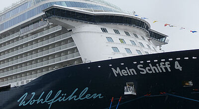 Auch die Mein Schiff 4 wird im Herbst nun um Afrika herum in ihr Winterrevier überführt Kreuzfahrtschiff mit dunkelblauem Bug und kunstvoller Aufschrift „Wohlfühlen“