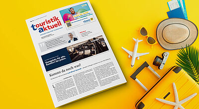 Ein gelbes Urlaubsszenario mit einer Ausgabe der Fachzeitung „touristik aktuell“ auf einem gelben Hintergrund. Neben der Zeitung liegen eine gelbe Sonnenbrille, ein Strohhut, ein Modellflugzeug, ein Reisepass mit Bordkarten, eine Kamera, eine gelbe Reisetasche mit einem Seestern darauf und ein Palmenblatt – Symbolik für Sommer, Reisen und Tourismus.