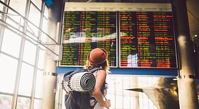 Frau mit Rucksack vor Anzeigentafel am Flughafen