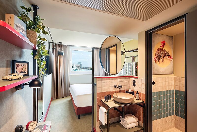 Das Me and All Hotel Berlin East Side will mit einem kompakten Zimmermodell überzeugen. Foto: Hyatt Modernes Hotelzimmer im Me and all Hotel Berlin East Side mit stilvoller Einrichtung, komfortablem Bett, offenem Waschbereich, Design-Details und Ausblick über Berlin