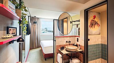 Modernes Hotelzimmer im Me and all Hotel Berlin East Side mit stilvoller Einrichtung, komfortablem Bett, offenem Waschbereich, Design-Details und Ausblick über Berlin