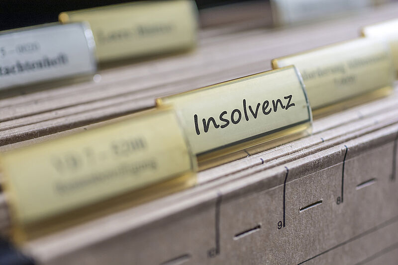 Nahaufnahme eines Aktenregister-Reiters mit der Beschriftung "Insolvenz" in einem Aktenschrank, unscharfer Hintergrund.
