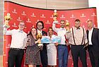 Fünf Männer und zwei Frauen auf einer Bühne vor einer Wand mit Emirates-Logos. Drei der Männer und eine Frau halten Goldene Trophäen in der Hand. 