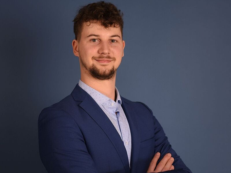 Porträt von Jakob Rühl, Mitarbeiter bei Eniyan, in blauem Sakko vor blauem Hintergrund – professionelles Businessfoto für Presse und Unternehmenskommunikation