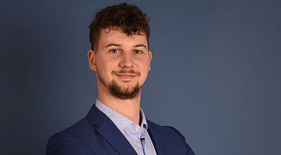 Porträt von Jakob Rühl, Mitarbeiter bei Eniyan, in blauem Sakko vor blauem Hintergrund – professionelles Businessfoto für Presse und Unternehmenskommunikation