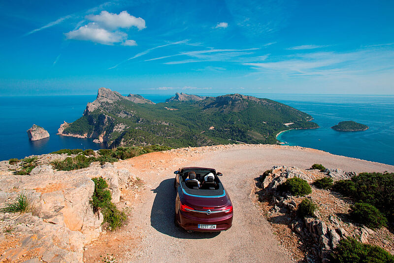 Mietwagen auf einer sonnigen Urlaubsinsel vor einer Kurve mit Blick aufs Meer