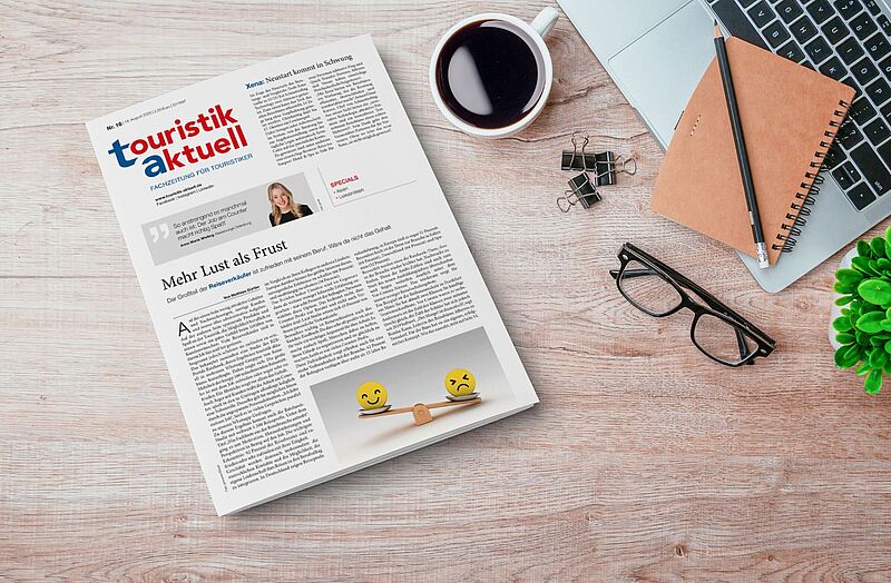 Die Ausgabe einer Fachzeitung für Touristik, platziert auf einem Schreibtisch mit typischen Arbeitsutensilien. Sie thematisiert unter anderem die Zufriedenheit von Reiseverkäufern und Branchenentwicklungen.