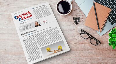 Die Ausgabe einer Fachzeitung für Touristik, platziert auf einem Schreibtisch mit typischen Arbeitsutensilien. Sie thematisiert unter anderem die Zufriedenheit von Reiseverkäufern und Branchenentwicklungen.
