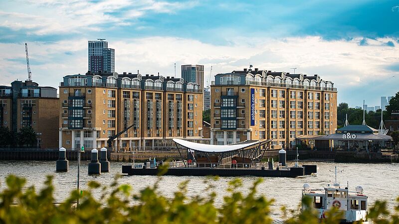 Moderner Gebäudekomplex des A & O Hostels direkt an der Themse in London mit Blick auf Fluss, Anlegestelle und vorbei fahrenden Booten