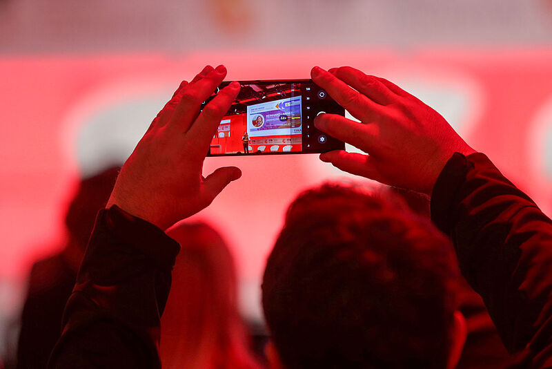 Etwa 400 internationale Experten werden auf den Bühnen des ITB Kongresses diskutieren Mann fotografiert mit Handy Menschen auf einer rot beleuchteten Bühne