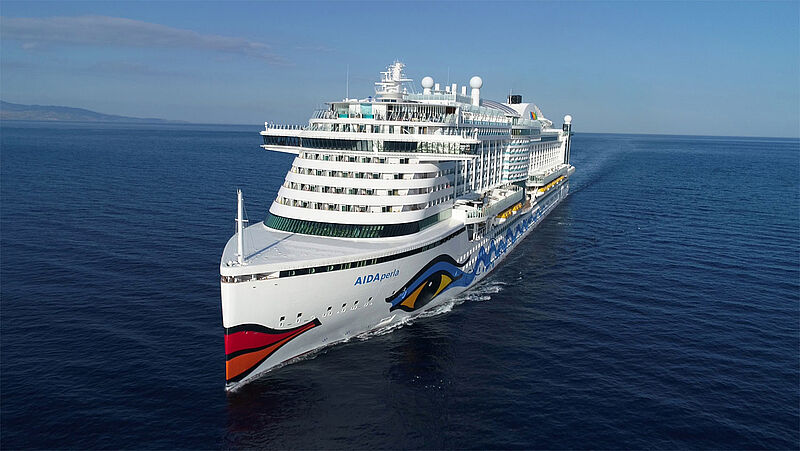 Das Kreuzfahrtschiff Aida Perla mit dem charakteristischen roten Kussmund am Bug und einem blau-gelbem Auge am seitlichen Rumpf fährt über dunkelblaues Meer. 