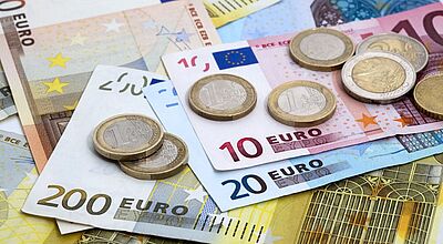 Verschiedene Euro-Banknoten und -Münzen, gestapelt und verteilt