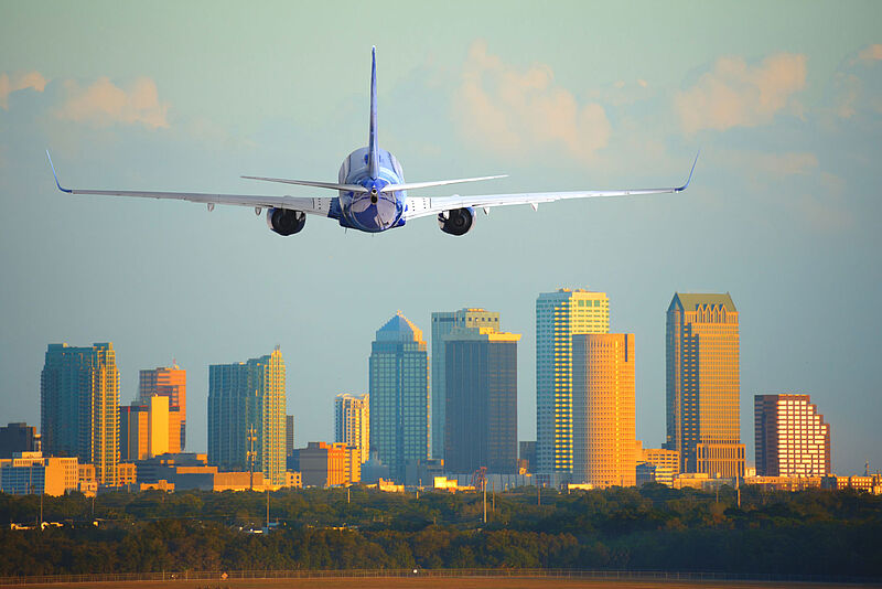 Landeanflug auf Tampa in Florida: Im US-Flugverkehr werden viele Streichungen erwartet Ein Flugzeug ist im Landeanflug vor Skyline einer US-amerikanischen Großstadt Vorfeld zu sehen. Die Hochhäuser werden vom warmen Licht der tiefstehenden Sonne angeleuchtet.