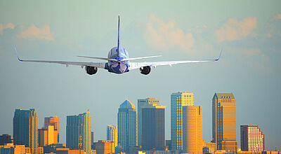 Landeanflug auf Tampa in Florida: Im US-Flugverkehr werden viele Streichungen erwartet Ein Flugzeug ist im Landeanflug vor Skyline einer US-amerikanischen Großstadt Vorfeld zu sehen. Die Hochhäuser werden vom warmen Licht der tiefstehenden Sonne angeleuchtet.
