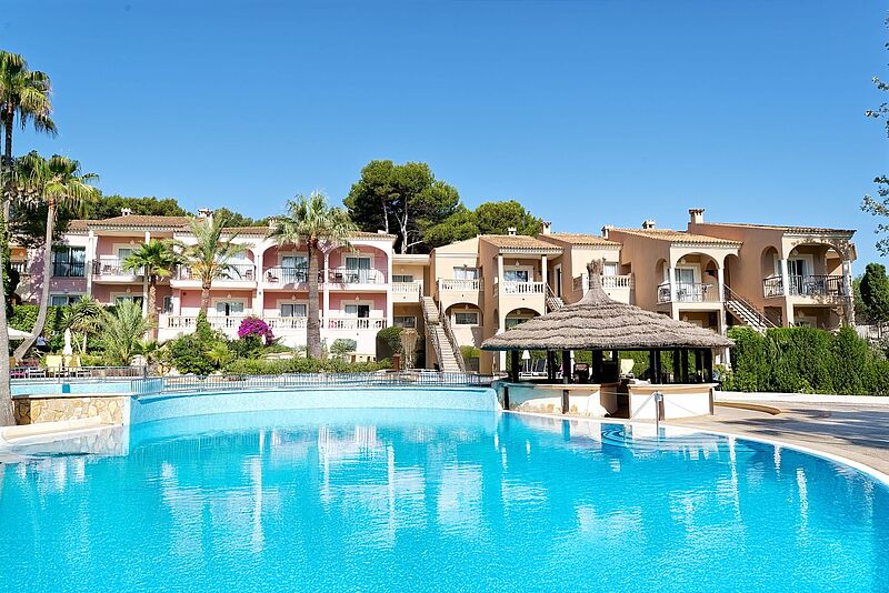 Mediterranes Hotel auf Mallorca mit palmengesäumtem Außenpool und Sonnenterrasse – entspannter Urlaub auf den sonnigen Balearen.
