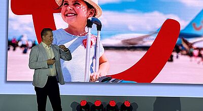 Ein Mann steht vor einer Wand mit dem TUI-Smiley