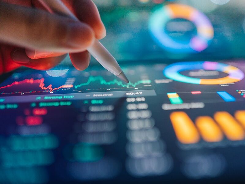 Durch einen automatisierten Datenaustausch werden bei Traffics künftig nicht verfügbare Hotels in Echtzeit aussortiert. Eine Hand hält einen digitalen Stift über einem leuchtenden Tablet, auf dem farbige Diagramme, Kurvenverläufe und Datenvisualisierungen angezeigt werden.