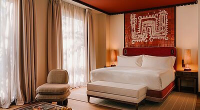 Blick in ein gepflegtes Hotelzimmer mit großem Bett und einer Ablage davor.