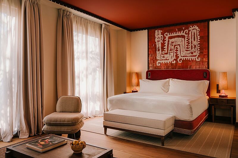 Blick in ein gepflegtes Hotelzimmer mit großem Bett und einer Ablage davor.