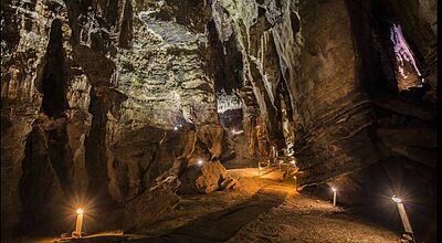 Beleuchteter Wanderweg in Tropfsteinhöhle mit dramatischen Felsformationen, Stalaktiten und atmosphärischer Beleuchtung durch Laternen