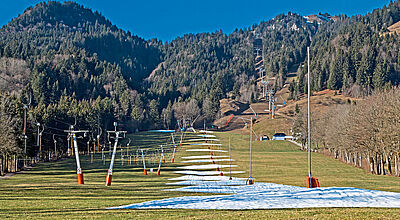 Berg mit grüner Wiese und Liftanlage mit wenig Kunstschnee