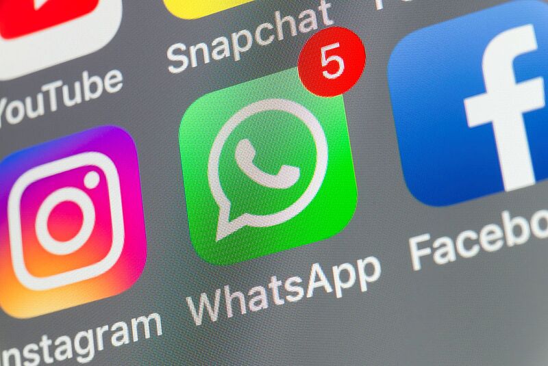 Nahaufnahme eines Smartphone-Bildschirms mit mehreren Social-Media-Apps. Im Fokus steht das grüne WhatsApp-Symbol mit einer roten Benachrichtigung („5“) oben rechts. Daneben sind die Logos von Instagram, YouTube, Snapchat und Facebook zu sehen.