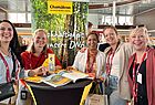 Fünf Frauen an einem Stand blicken in die Kamera und lachen