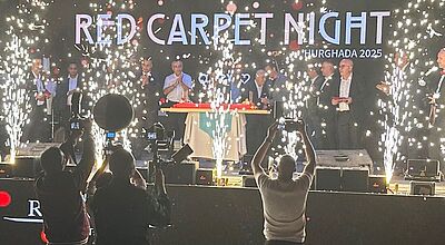 Der Galaabend zur Red Carpet Night fand im Rixos Magawish in Hurghada statt Bühnenaufnahme einer feierlichen Veranstaltung mit großem Feuerwerkseffekt. Auf der beleuchteten Bühne stehen mehrere Personen in formeller Kleidung hinter einem Tisch, während Funkenfontänen links und rechts hochschießen. Im Vordergrund fotografieren und filmen mehrere Personen die Szene. Auf der Bühnenrückwand steht groß „Red Carpet Night – Hurghada 2025“.