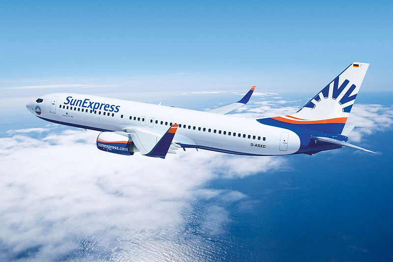 Ein Flugzeug von Sun Express fliegt vor blauem Himmel und bei Sonnenschein über Wolken und dem Meer