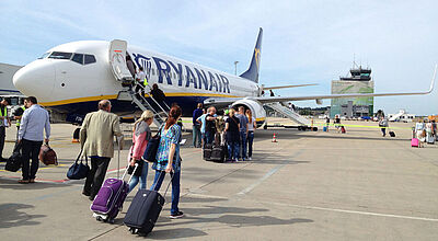 Passagiere mit Rollkoffern gehen auf dem Vorfeld des Flughafens Frankfurt-Hahn zu einer Maschine von Ryanair, um dort einzusteigen.
