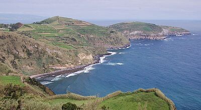 Atemberaubende Steilküste mit grünen Hügeln und Terrassenfeldern auf Sao Miguel, Azoren, Portugal – Blick auf das tiefblaue Atlantikmeer mit sanften Wellen.