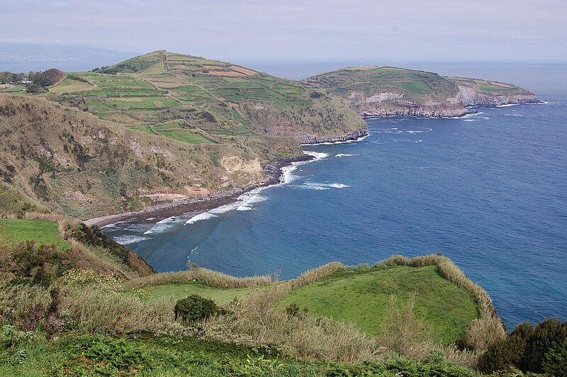 Atemberaubende Steilküste mit grünen Hügeln und Terrassenfeldern auf Sao Miguel, Azoren, Portugal – Blick auf das tiefblaue Atlantikmeer mit sanften Wellen.