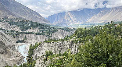Gebirgslandschaft mit türkisfarbenem Fluss, steilen Felswänden, Pappeln und grünen Siedlungsterrassen im pakistanischen Hunza-Tal