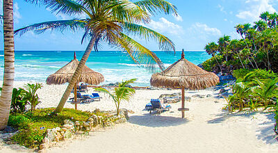 Weißer feinsandiger Strand mit Liegestühlen, im Hintergrund das Meer